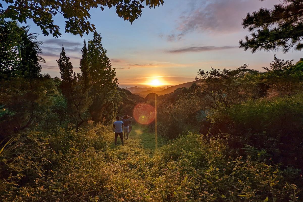 兩個人站在山坡的草徑上看夕陽,遠處是一層一層的山