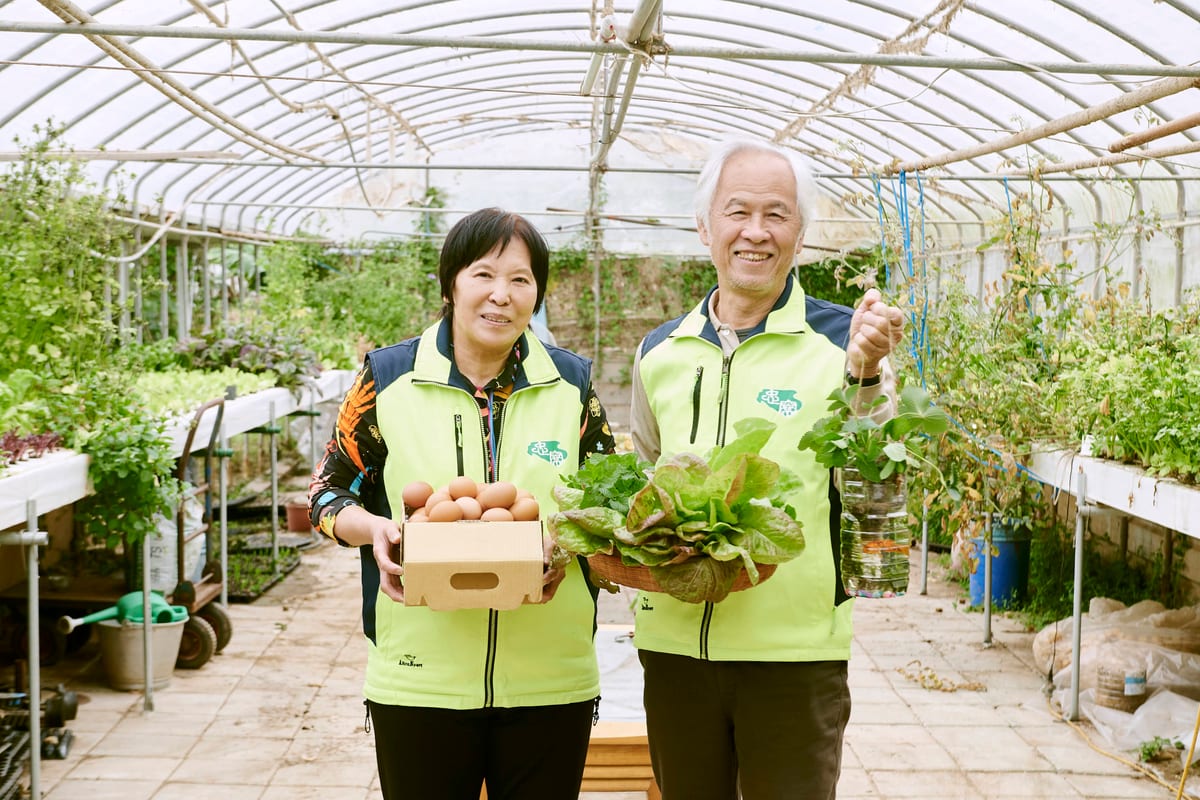 兩位農友站在溫室走道上,手裡捧著自己種的菜