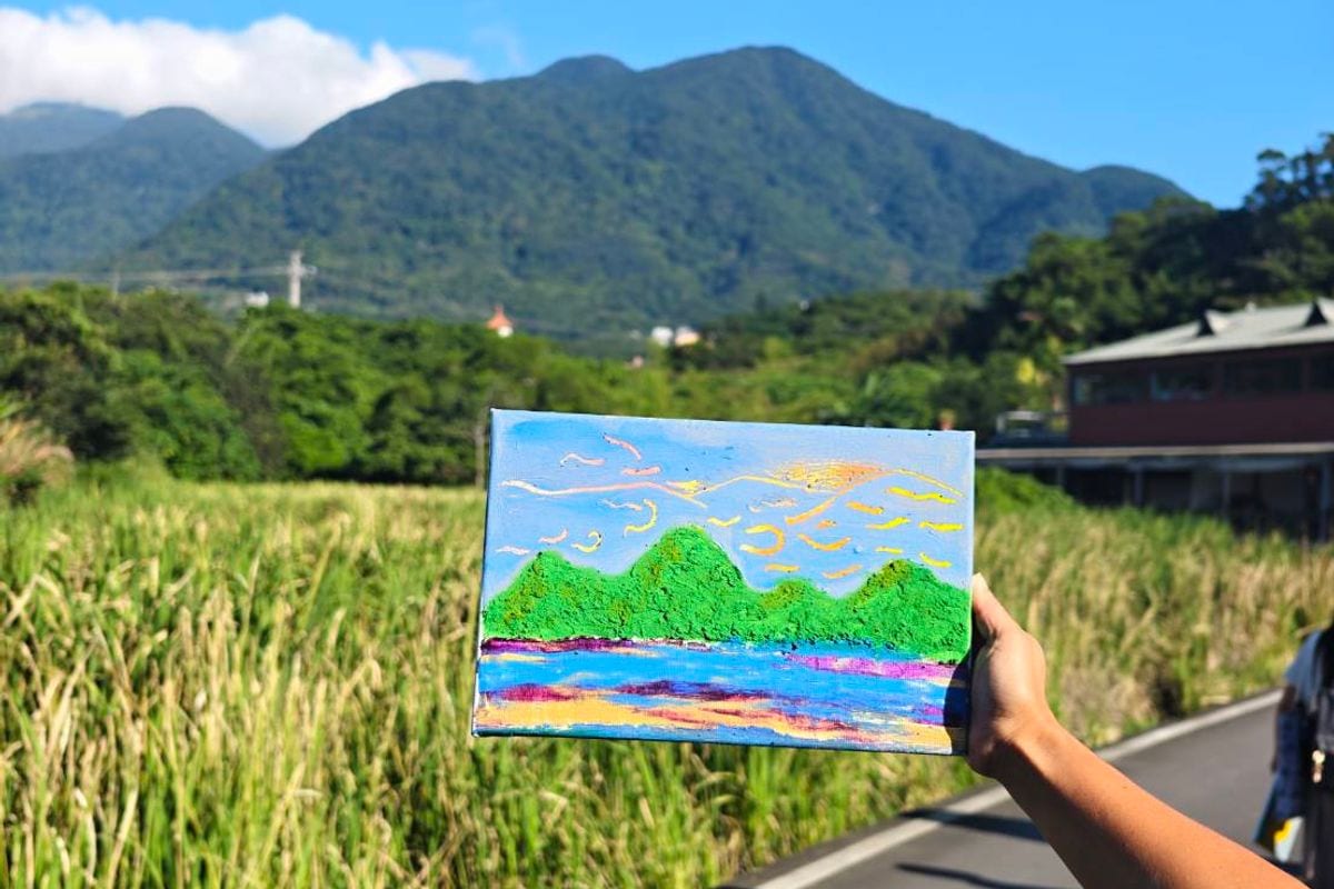 有人把剛畫好的畫舉起來，對著遠處真的那座山