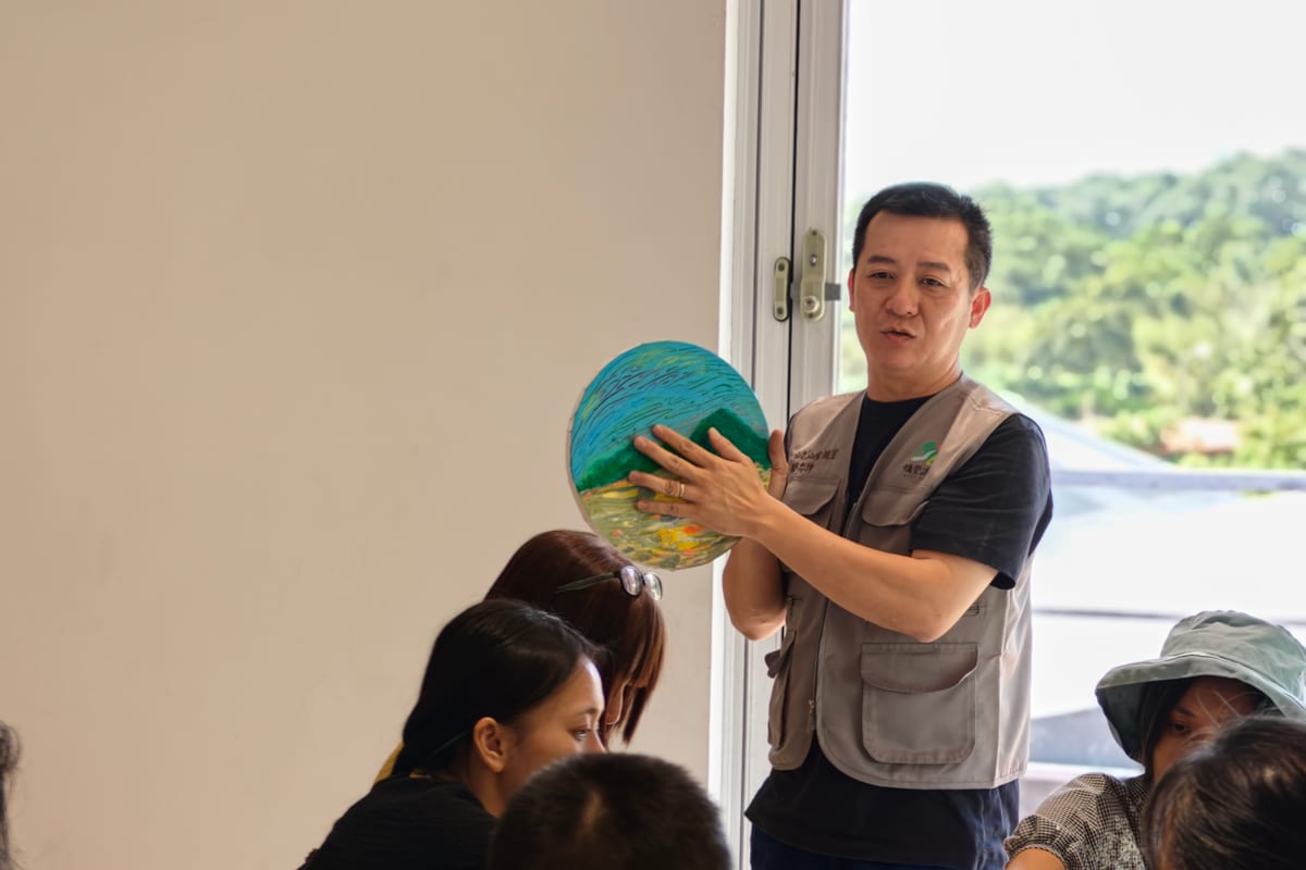 帶畫畫的老師舉著一張圓形的畫，向圍坐的學員說明